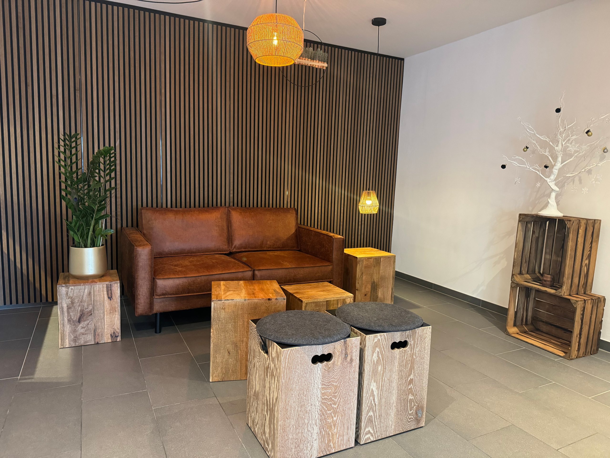 Lounge-Ecke bei Vinori mit braunem Ledersofa, Holzlamellenwand, Holzkisten als Tische und Pendelleuchten