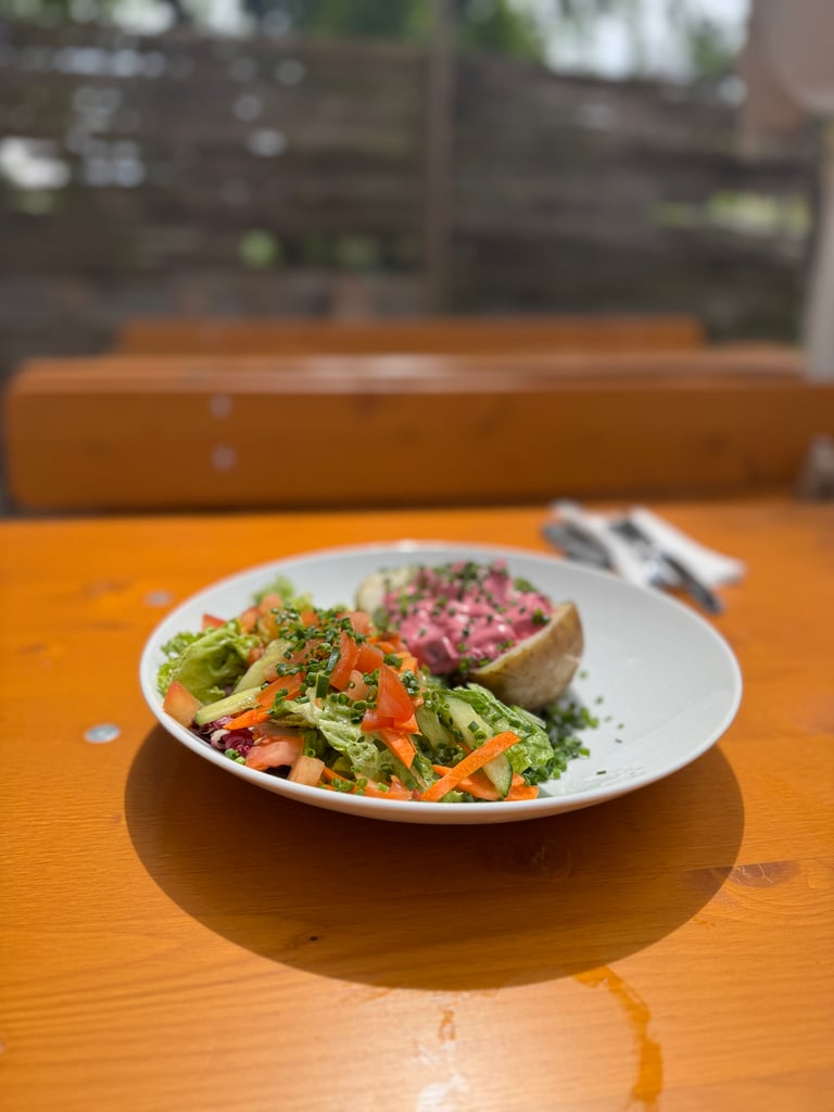 Plate of colorful mixed salad on a white dish, with tomatoes, greens, and herbs, on a wooden table outdoors.