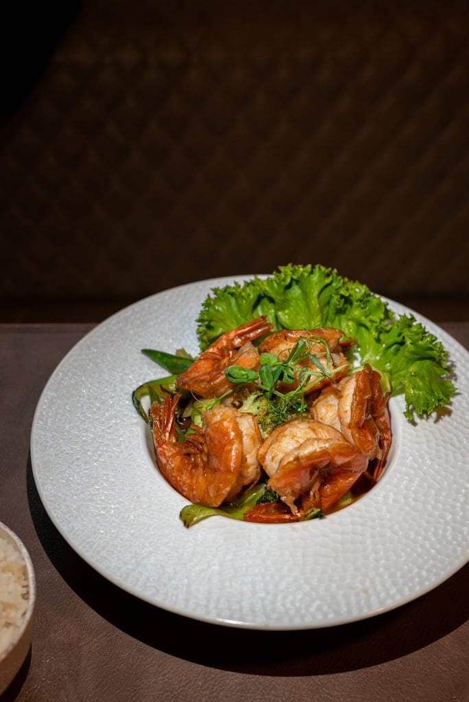 Plate of cooked shrimp arranged over greens with lettuce garnish on a textured white plate.