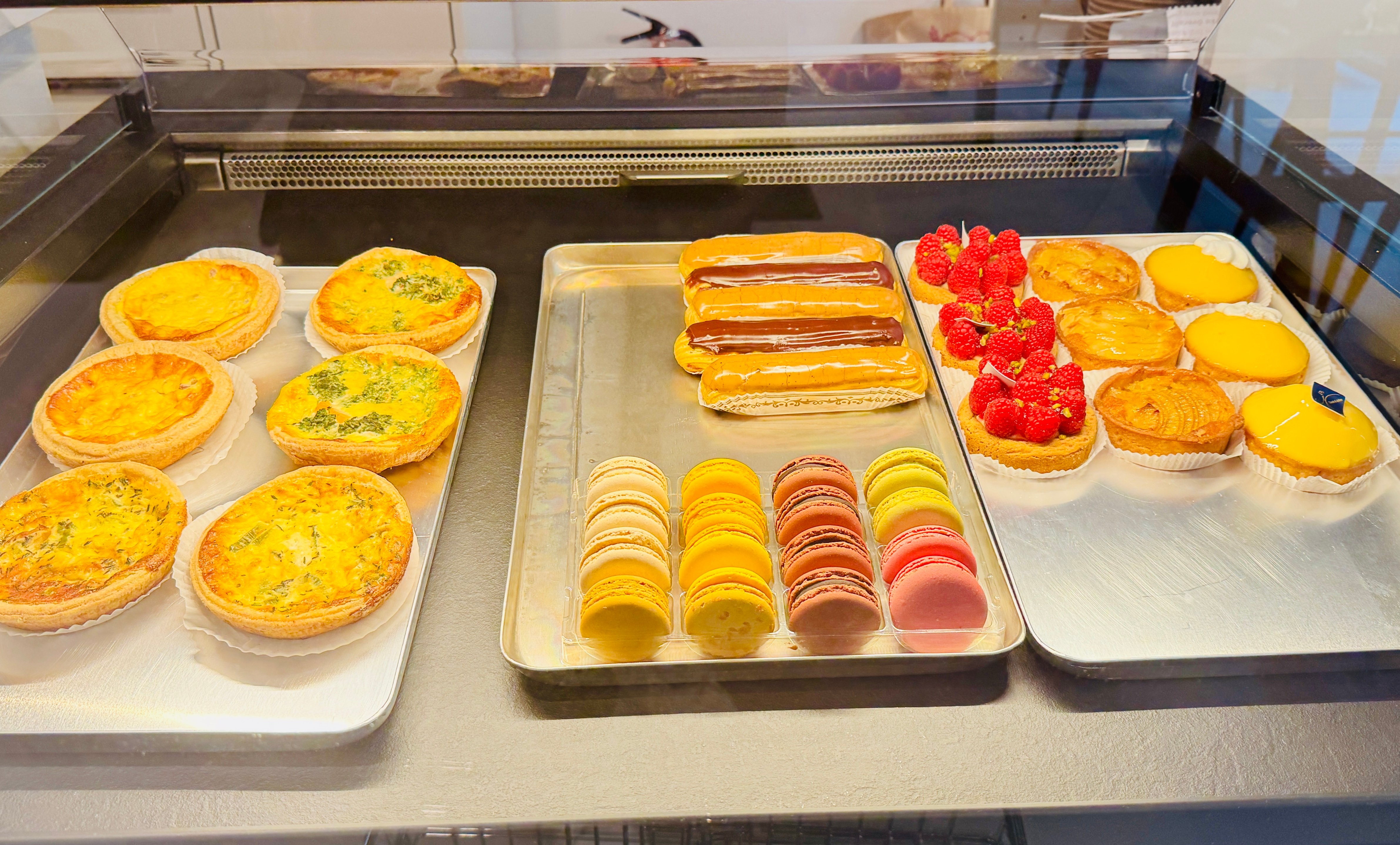 Theke mit Quiches, Eclairs, Tartelettes und bunten Macarons