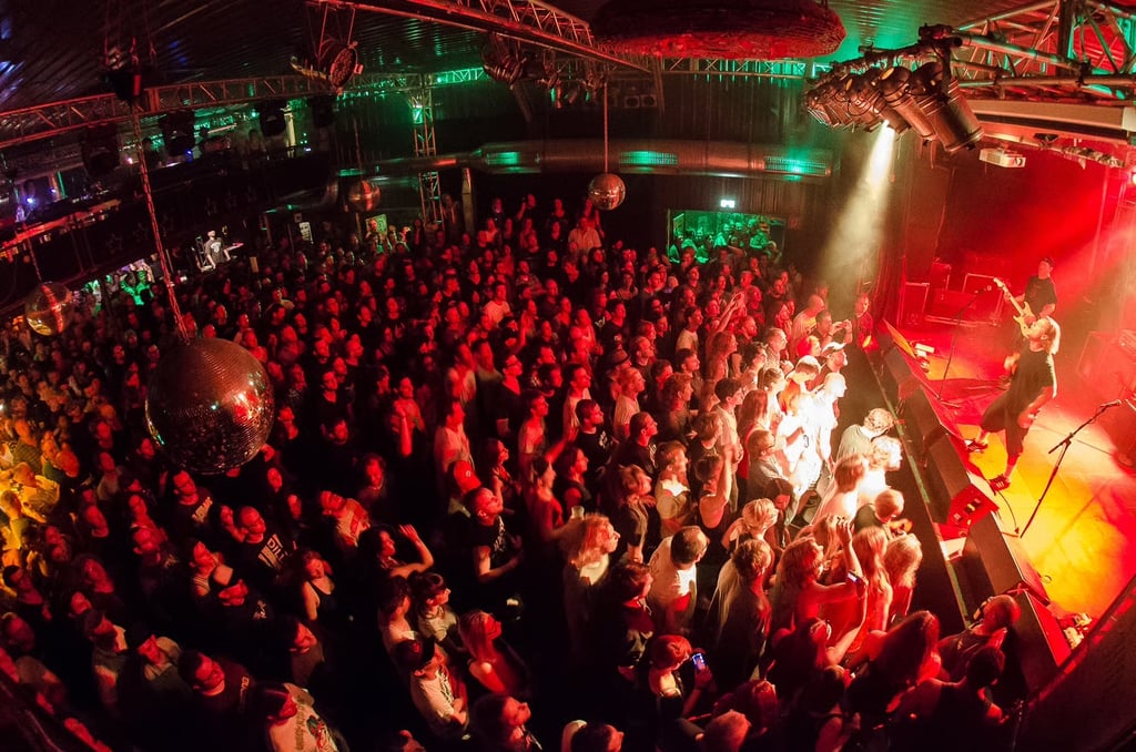 Large crowd at a live concert, performers on a red- and green-lit stage seen to the right.