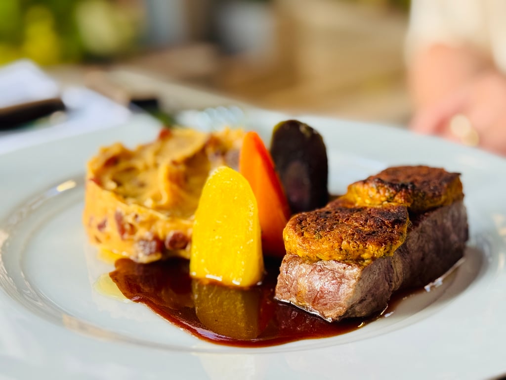 Beef medallions with roasted carrots and a glossy sauce on a white plate.