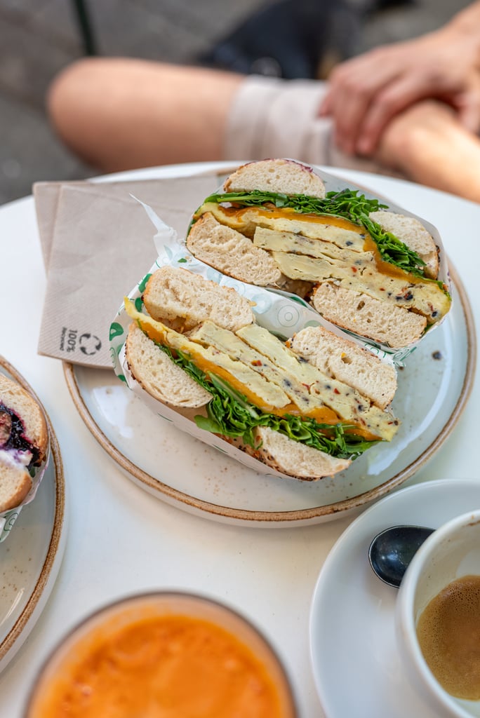 Club-style sandwich halves filled with greens and cheese on rustic bread, served on a plate with a napkin and a coffee cup nearby.