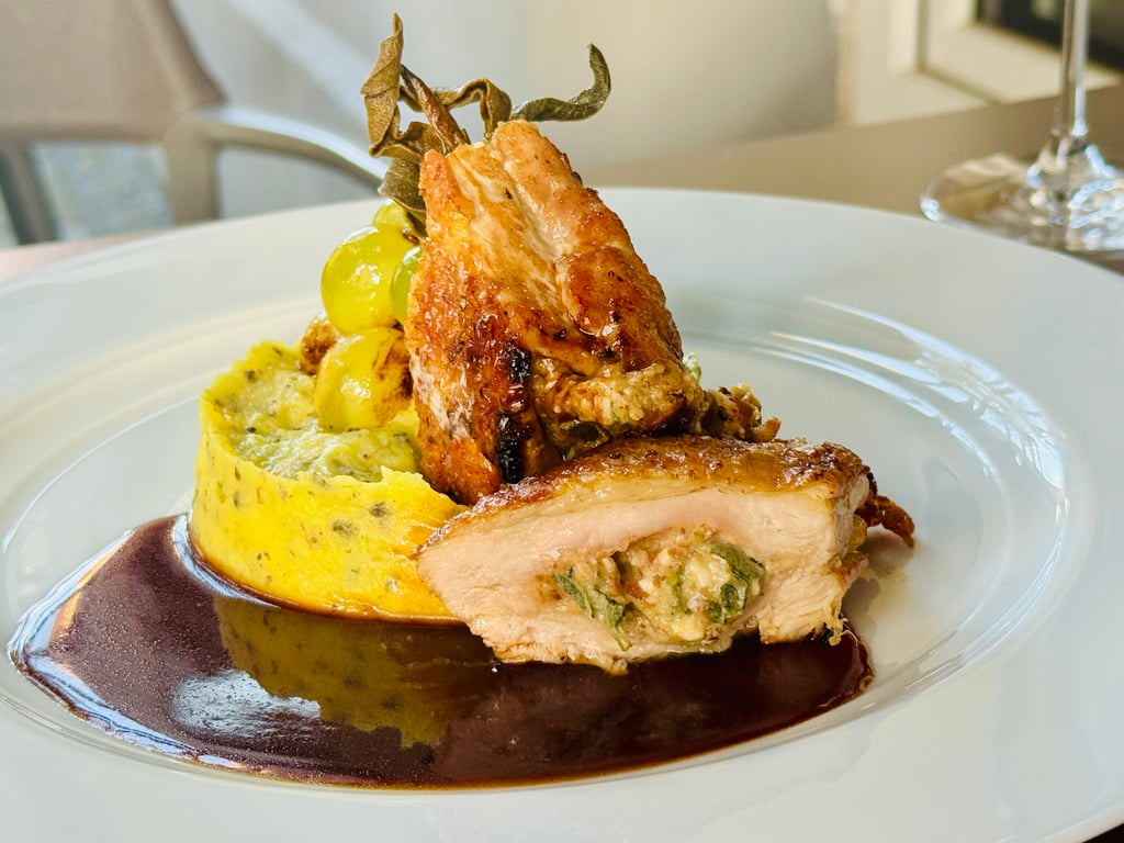 Roasted chicken leg served on creamy herb polenta with yellow vegetables and a glossy sauce on a white plate.