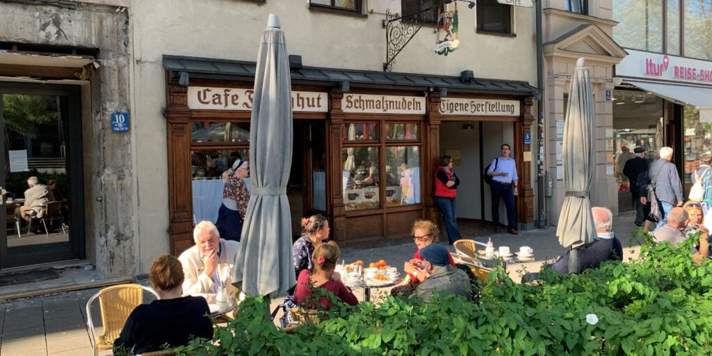 Terrasse vor dem Café Frischhut mit Sonnenschirmen und Gästen an kleinen Tischen