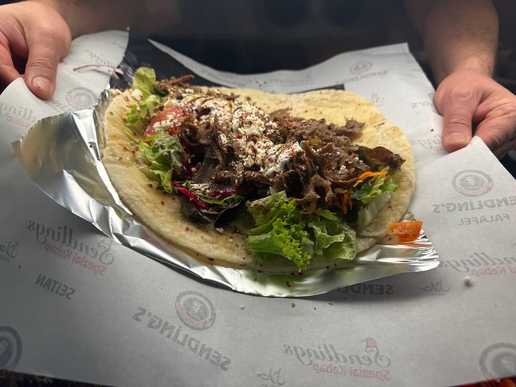 Beef gyro in a warm pita with lettuce, tomato, and crumbled cheese on a foil-lined plate.