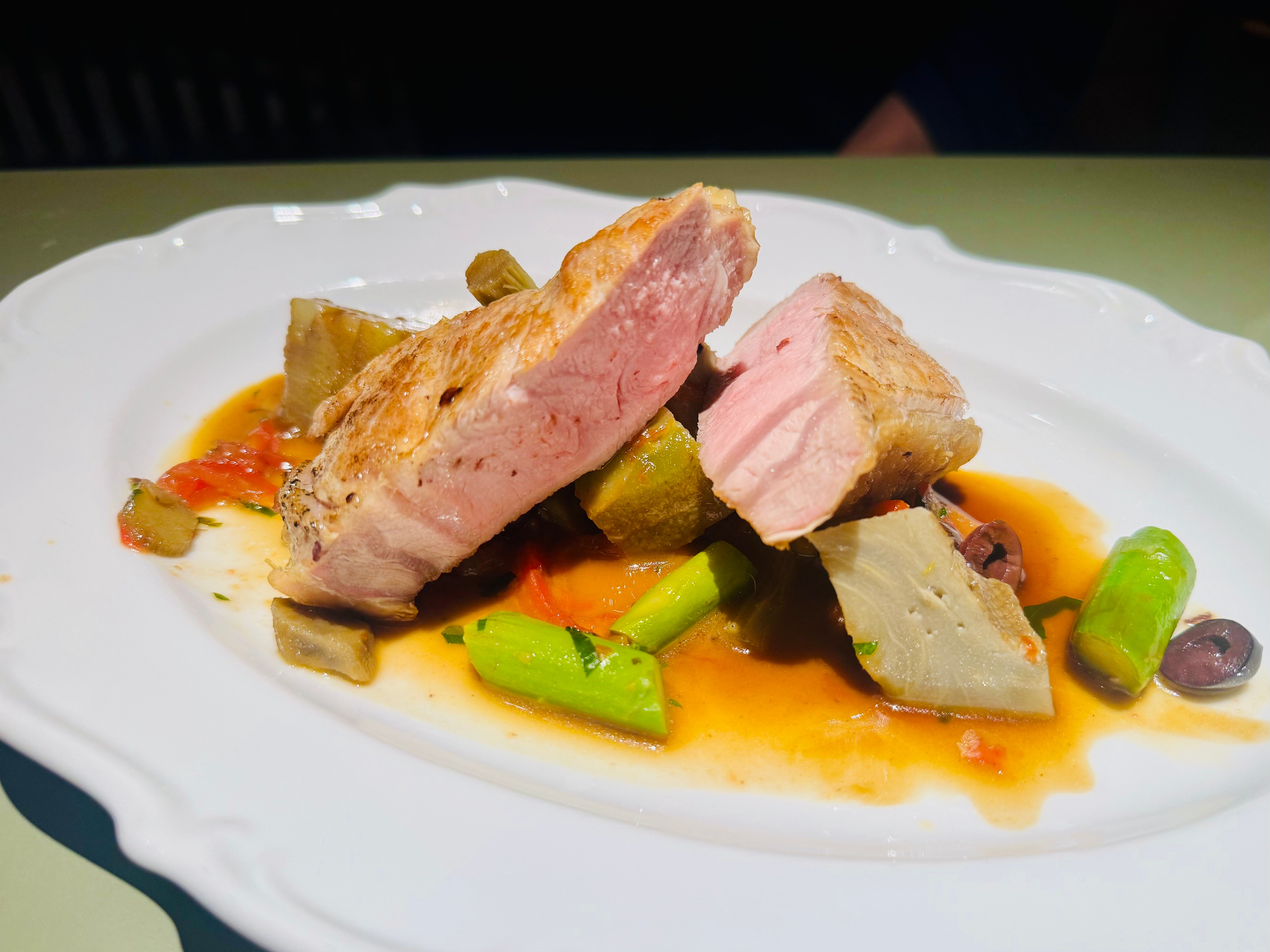 Rosa gebratenes Milchkalb mit geschmorten Artischocken, Tomaten und Oliven auf einem weißen Teller
