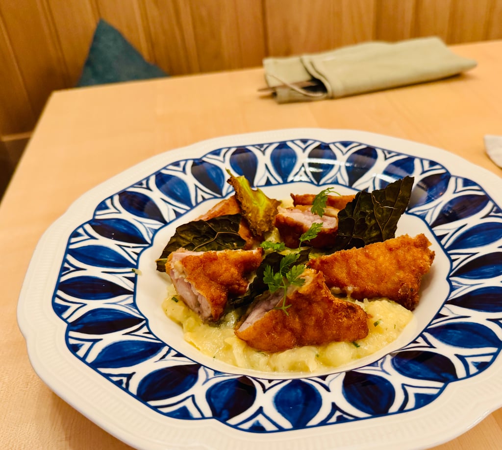 Plate with breaded fried fish or chicken pieces on a bed of creamy potatoes, garnished with herbs, on a blue patterned dish.
