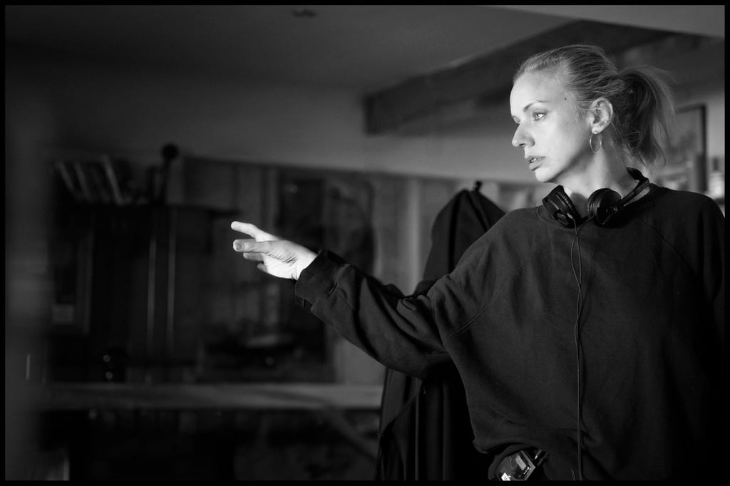 Woman in a dark sweatshirt with headphones around her neck, gesturing with her left hand in a studio setting.