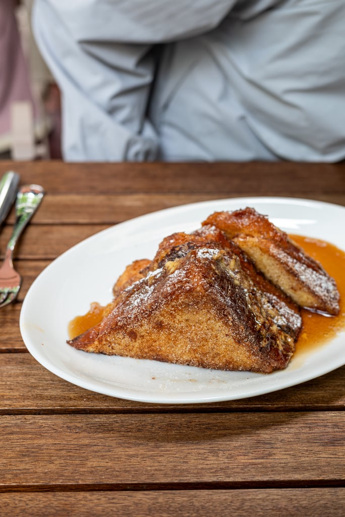 Plate of golden-brown French toast slices with syrup on a white plate, dusted with powdered sugar on a wooden table
