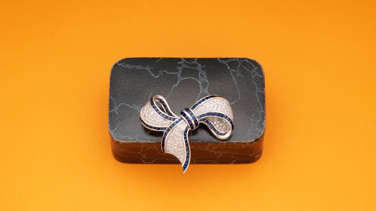 Black textured gift box with a sparkling silver-and-blue jeweled bow on an orange background.