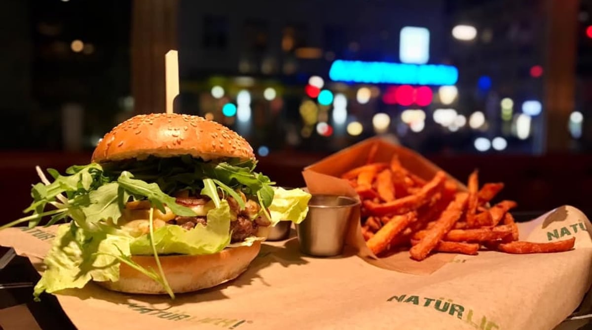 Burger mit Rucola und Süßkartoffelpommes vor dem Fenster, draußen die Lichter der Fraunhoferstraße