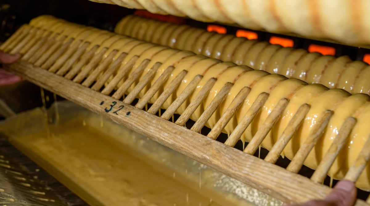 Baumkuchen dreht sich in der Backstube der Conditorei Kreutzkamm über der offenen Flamme, davor die Walze mit dem Teig