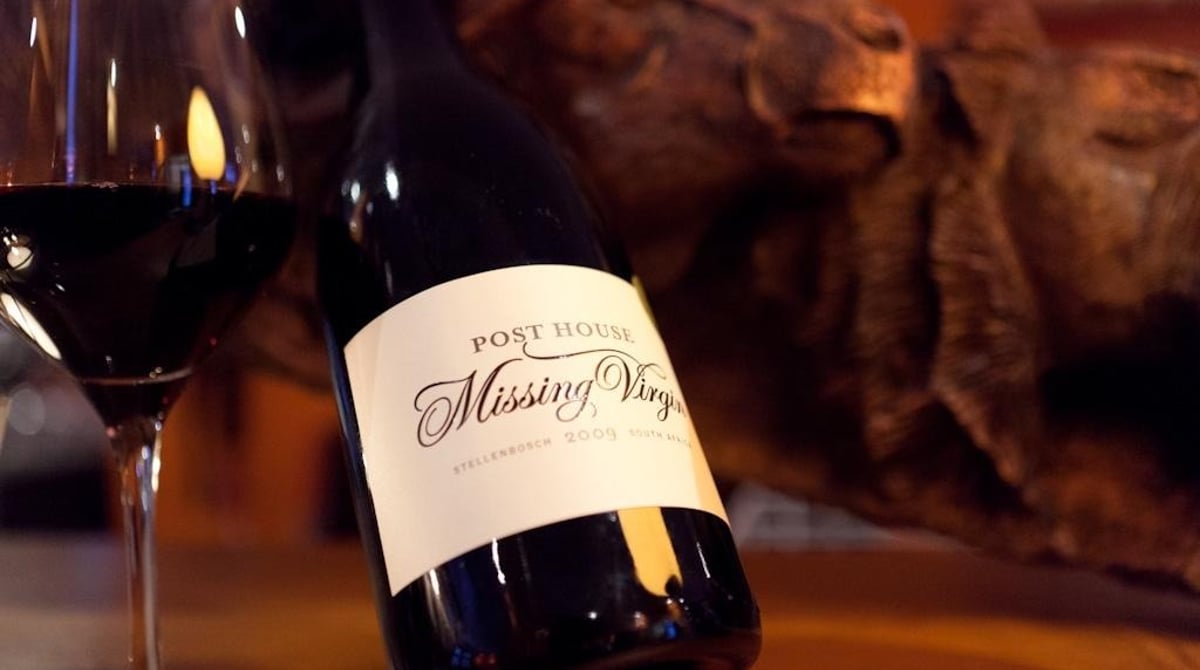 Glas Rotwein und Flasche Missing Virgin vom Kap auf einem Holztisch
