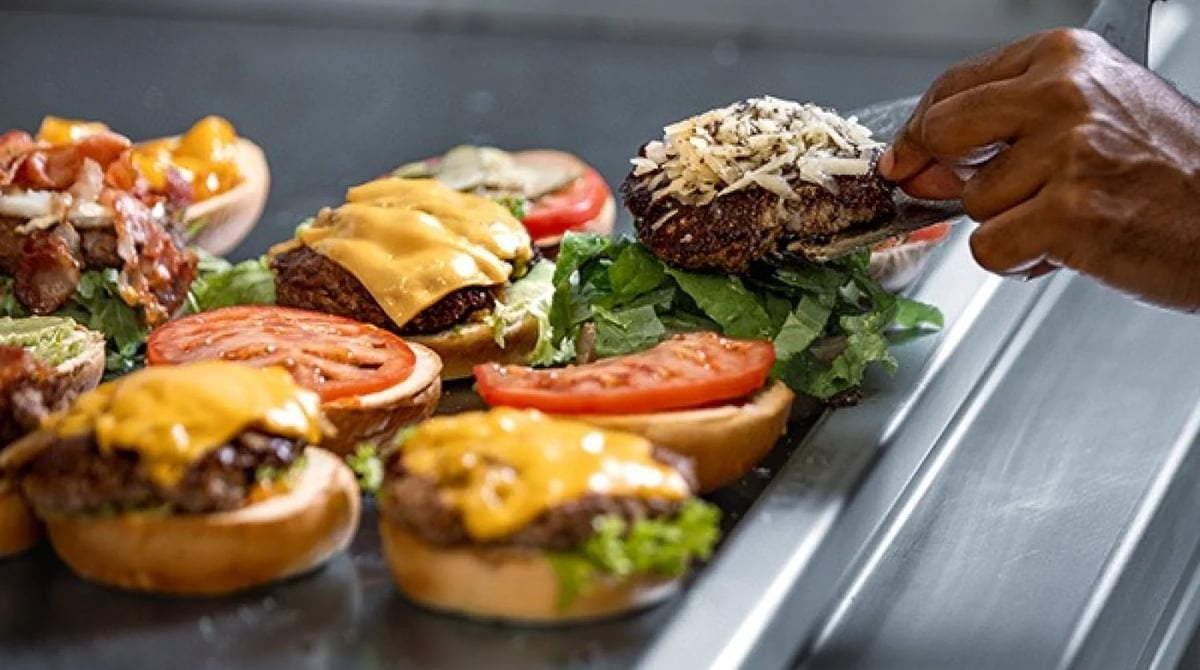 Mehrere Burger mit Cheddar, Tomate und Salat werden auf einer Arbeitsfläche angerichtet