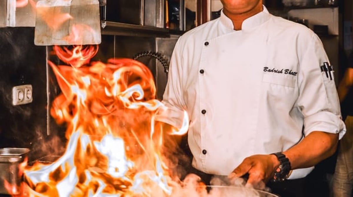 Koch am Herd mit hoch lodernder Flamme in der Küche des Indian Mango