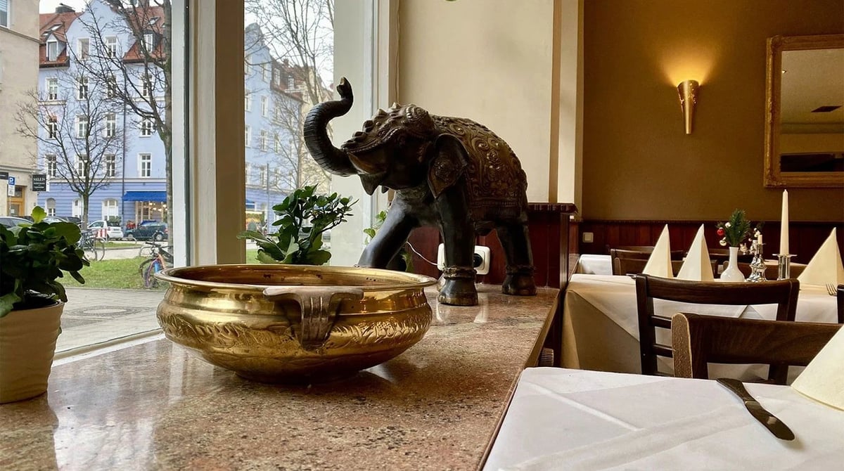 Messingschale und Elefantenfigur neben einem gedeckten Tisch im Gastraum des Bollywood in München-Neuhausen