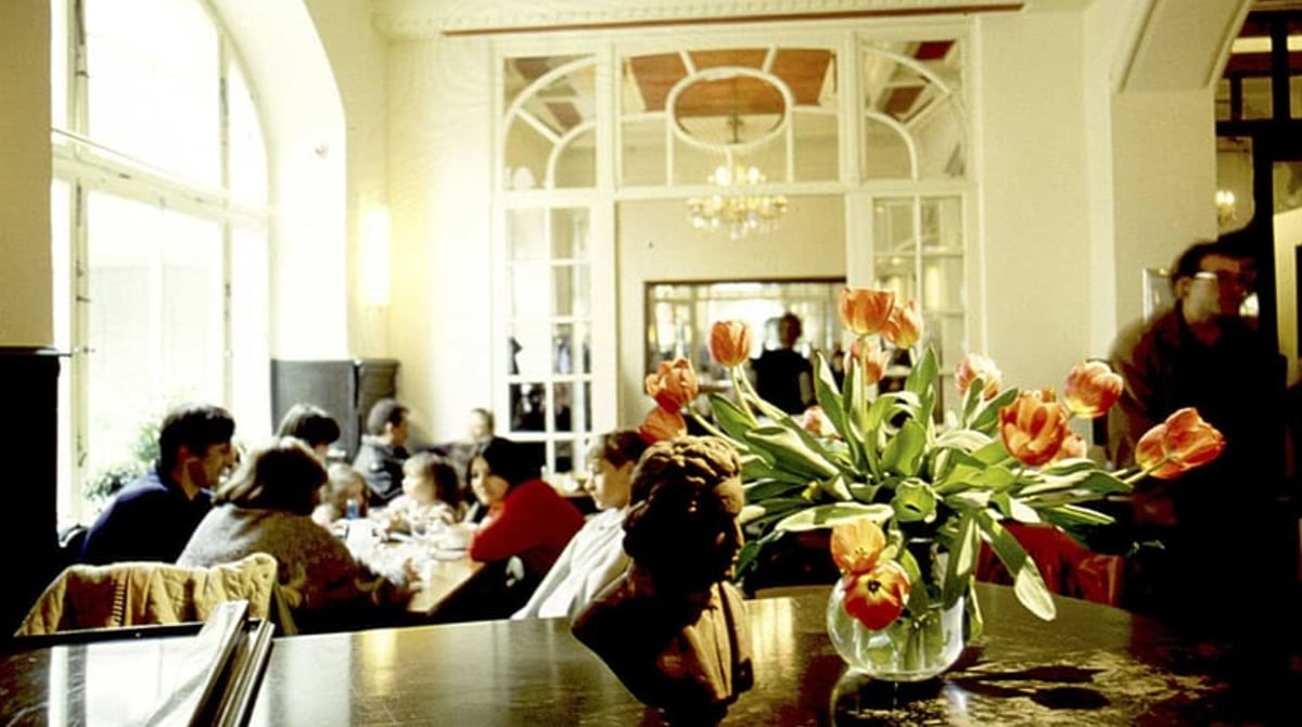 Gäste an den Tischen im Saal des Cafés, im Vordergrund ein Strauß Tulpen