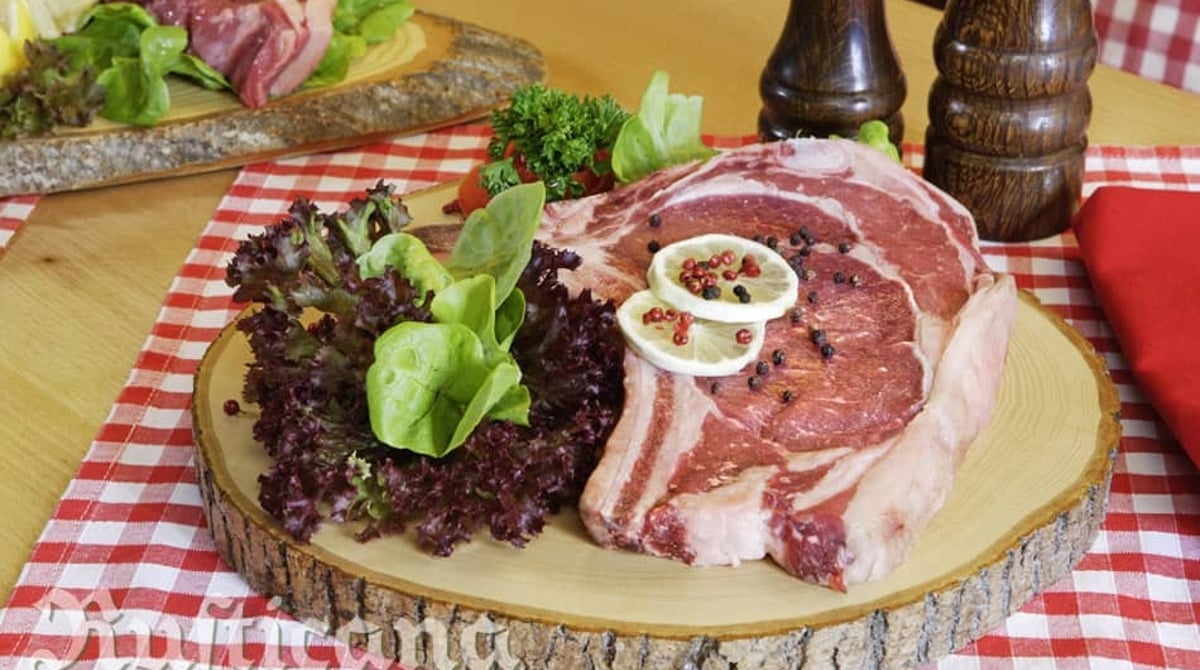 Rohes Rib-Eye auf einem Holzbrett mit Salat und Pfeffermühle