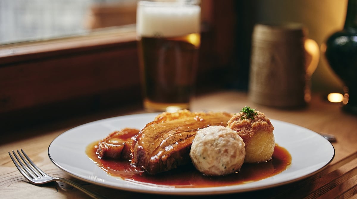Schweinsbraten mit Knödel und Soße auf einem Holzbrett