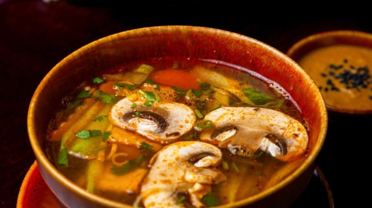 Klare Suppe mit Pilzen, Tofu und Gemüse in einer dunklen Schale
