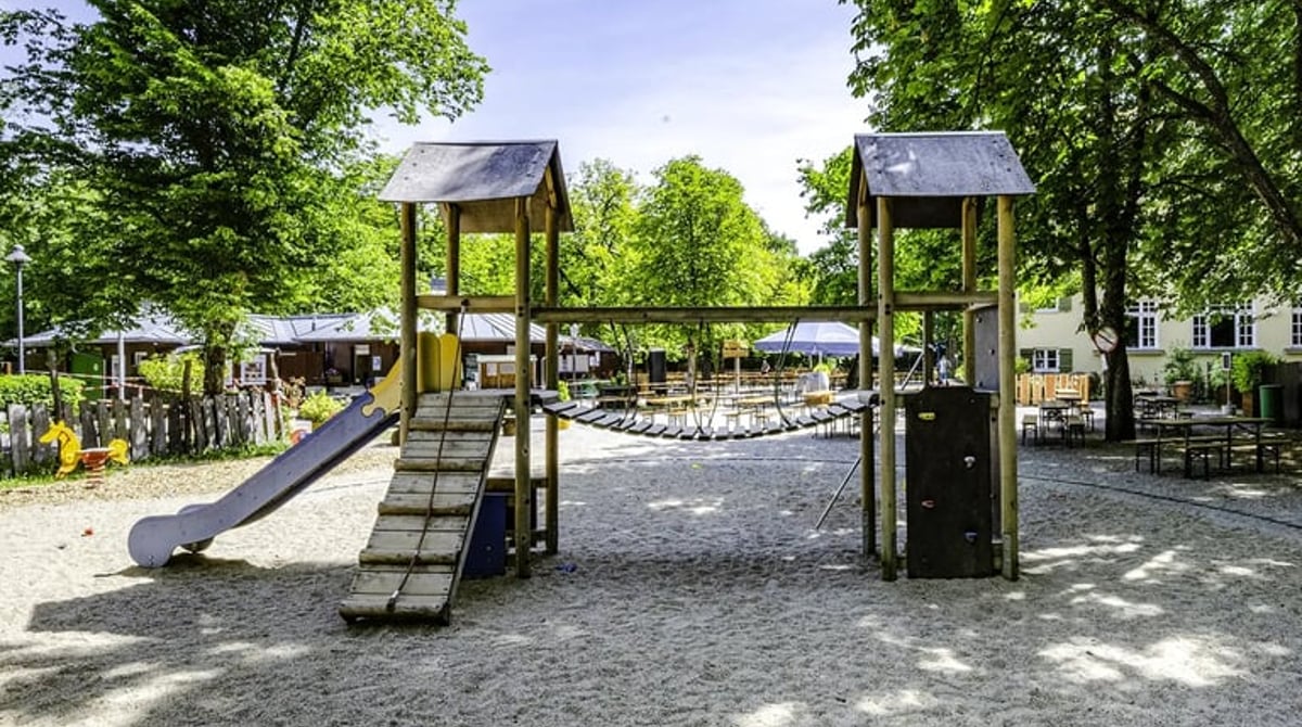 Spielplatz mit Rutsche und Klettergerüst zwischen hohen Bäumen