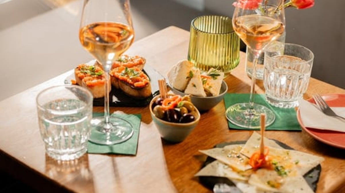 Gedeckter Tisch mit Pan con tomate, Manchego, Oliven und zwei Gläsern Weißwein
