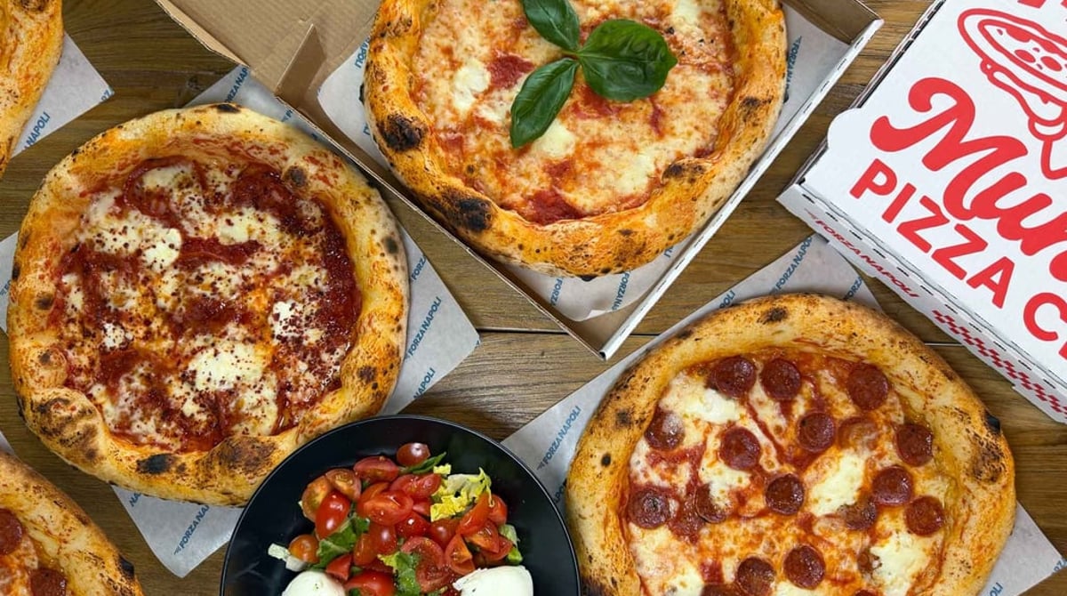 Drei Pizzen mit Büffelmozzarella in Kartons, ein Salat mit Mozzarella und ein Pizzakarton von Forza Napoli auf einem Holztisch