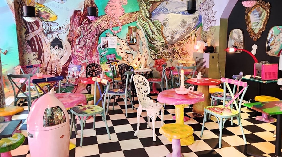 Bunt gestalteter Gastraum mit Schachbrettboden, rosa und gelben Möbeln und einem großen Wandbild