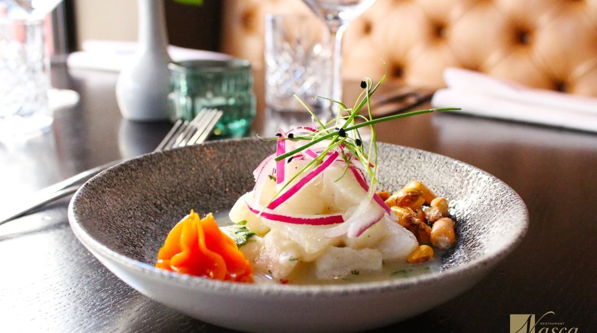 Ceviche Tradicional mit Fisch, roten Zwiebeln, Süßkartoffel und Cancha in einer grauen Schale auf einem gedeckten Tisch im Nasca
