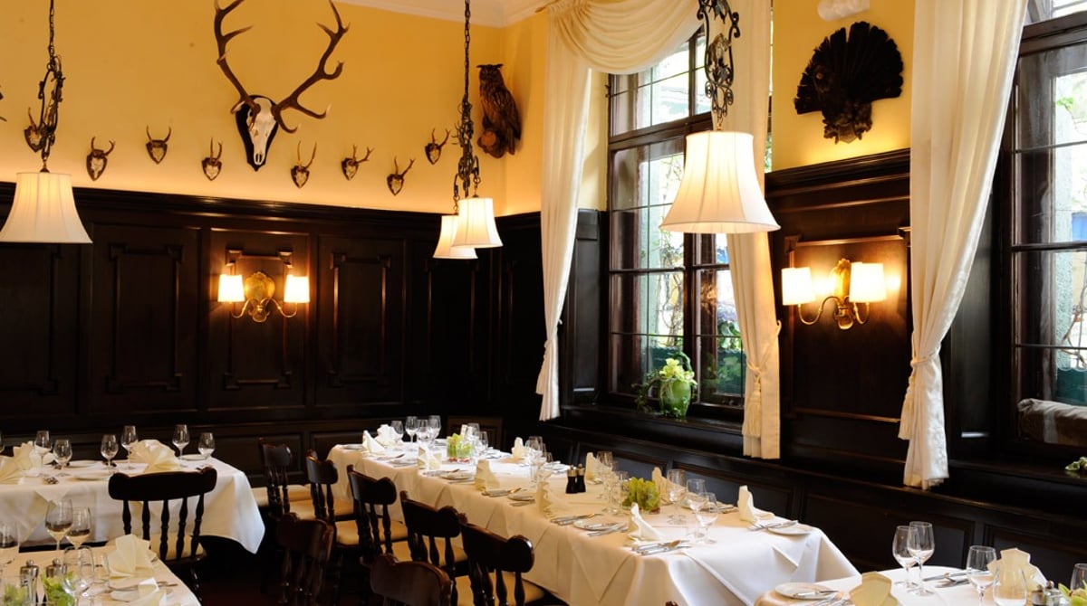 Gastraum des Halali mit dunkler Holzvertäfelung, Hirschgeweihen an der Wand und gedeckten Tischen