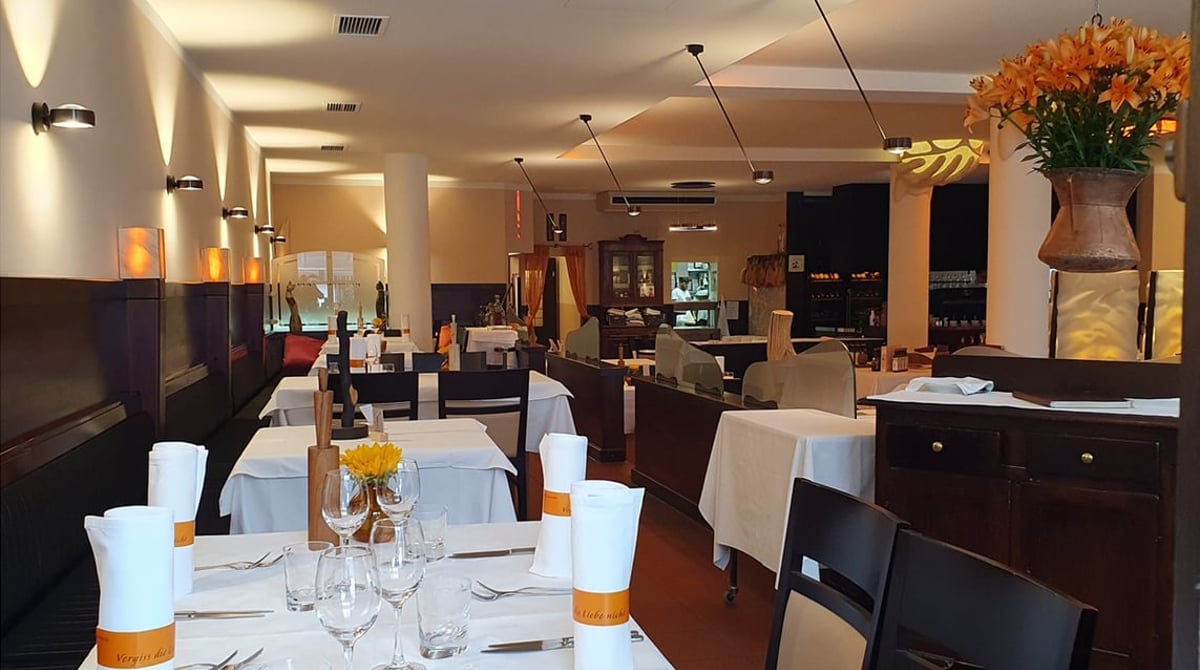 Langer Gastraum der Osteria der Katzlmacher mit gedeckten Tischen und Blumen