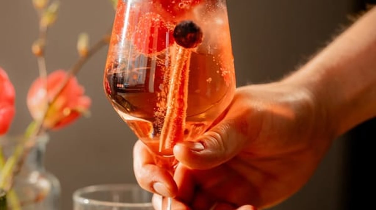 Hand hält ein Glas Lillet Wildberry mit Brombeeren