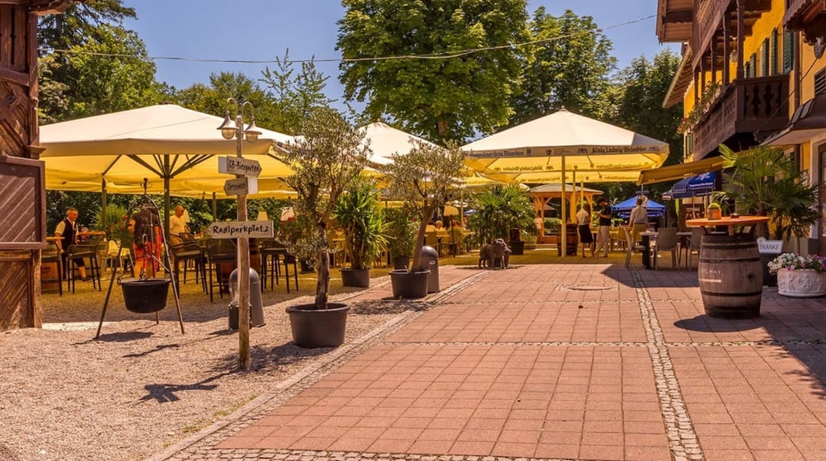 Seeterrasse des Gasthofs Hinterbrühl mit hellen Sonnenschirmen, Olivenbäumen und Kastanien