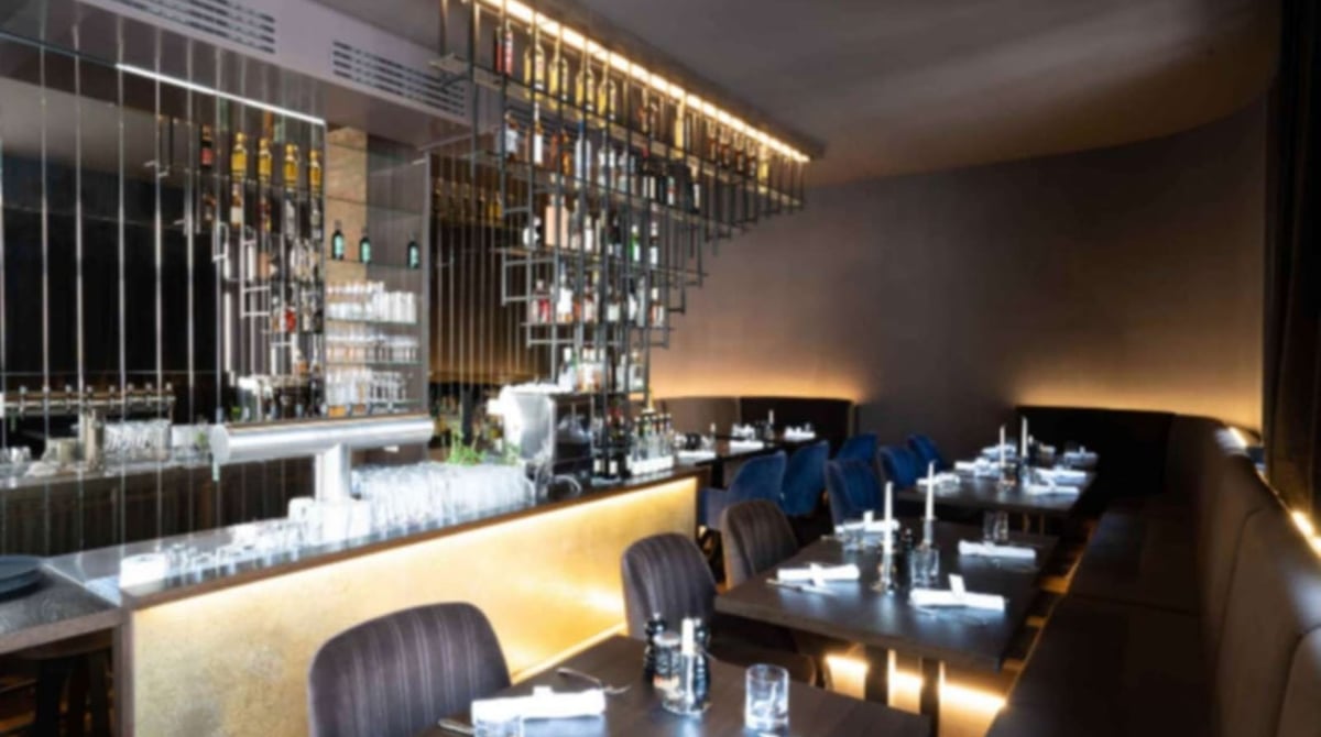Gastraum des Beefroom61 mit beleuchteter Bar, Flaschenregal und gedeckten Tischen