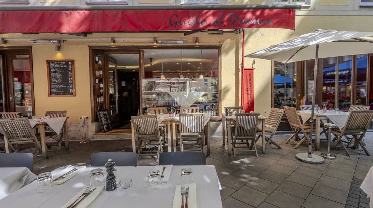 Eingang des Guido al Duomo am Frauenplatz mit gedeckten Tischen auf der Terrasse und roter Markise