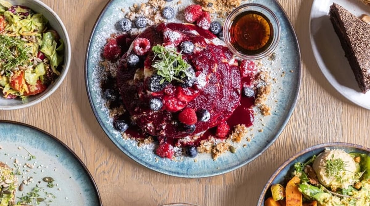 Pancakes mit Beeren, Bowls und ein Stück Kuchen auf einem Holztisch, von oben fotografiert