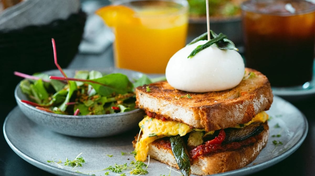Geröstetes Toskanabrot mit Rührei, Burrata und Salbei, dazu Salat und ein Glas Orangensaft