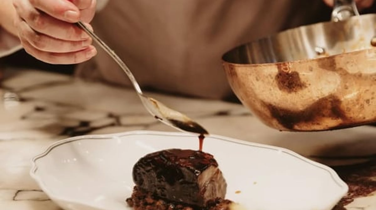 Köchin richtet ein Fleischgericht mit Sauce an, daneben ein Töpfchen Pommes frites