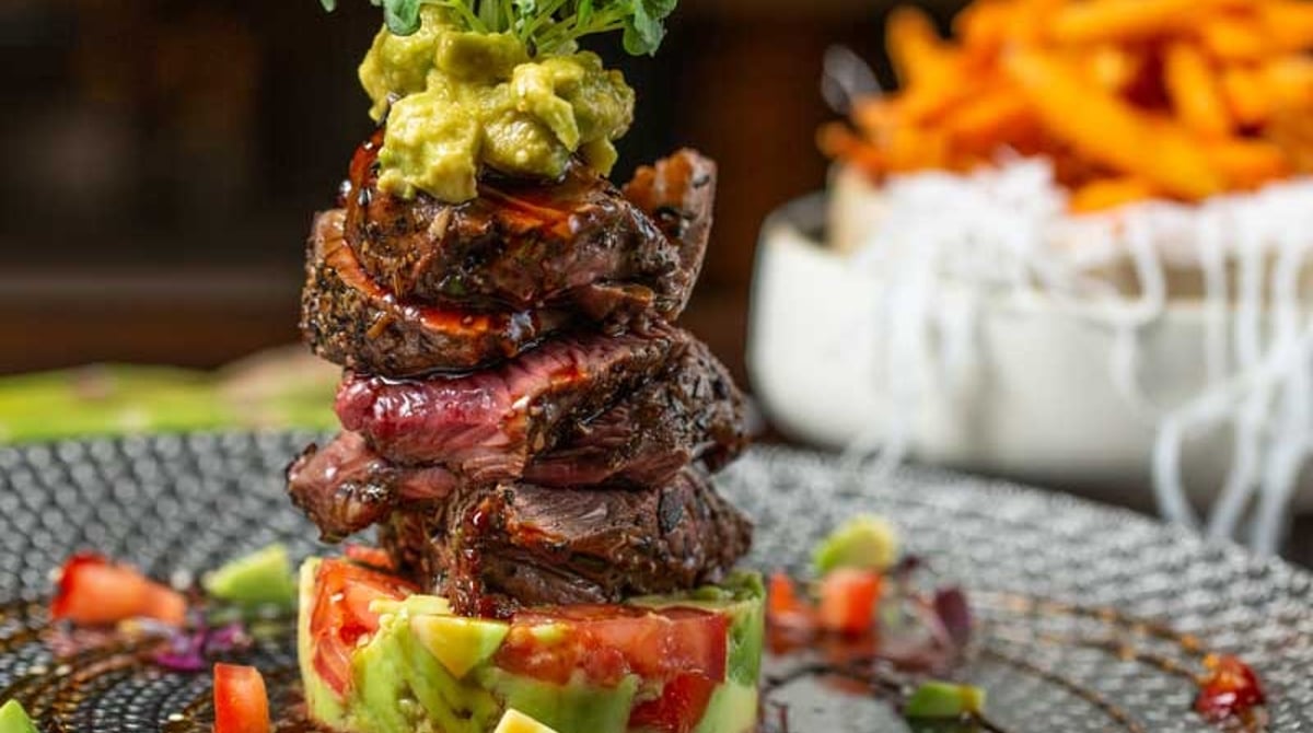 Angerichteter Teller mit Rindfleisch, Avocado und Tomaten, daneben Süßkartoffel-Pommes