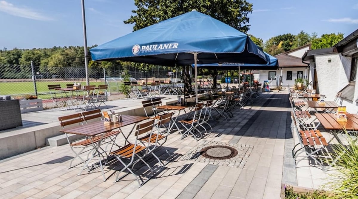 Gepflasterte Terrasse mit Holztischen und Klappstühlen unter blauen Schirmen