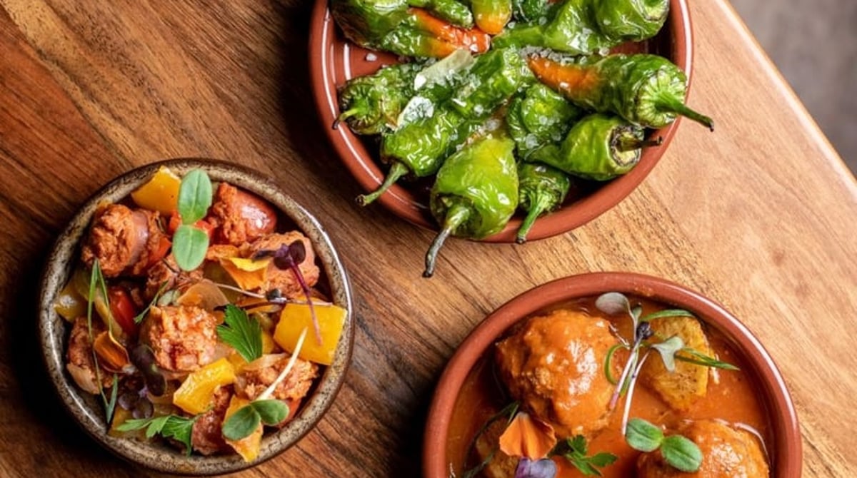 Pimientos de Padrón und Albóndigas in Tonschalen auf einem Holzbrett