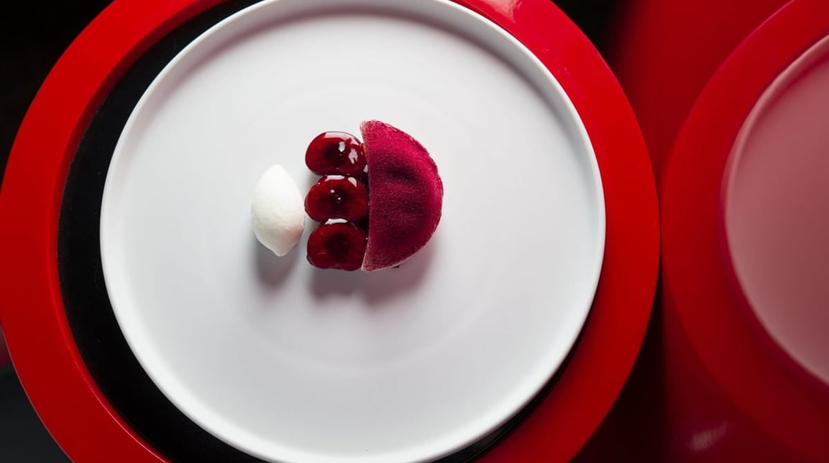 Dessert aus Kirschen und einer weißen Kugel auf einem weißen Teller mit rotem Rand