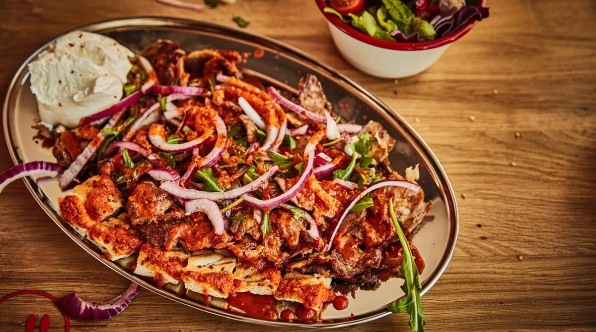 Döner-Teller mit Fleisch vom Spieß, roten Zwiebeln, Rucola und Joghurt auf einem Holztisch bei Hans Kebab