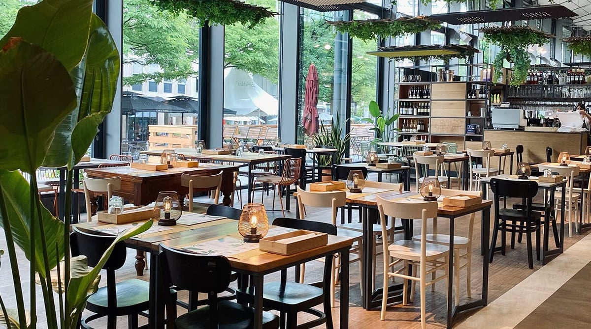 Gastraum des Restaurants bei Eataly mit Holztischen, Pflanzen und großen Fenstern