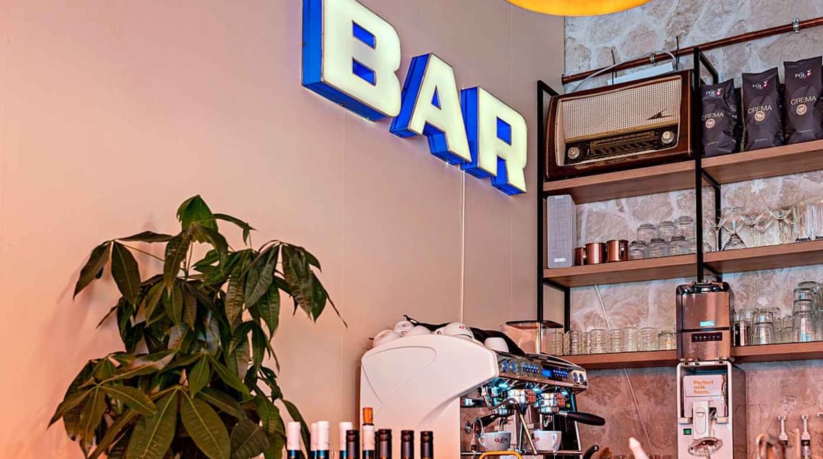 Theke der ORA Tagesbar mit blauem BAR-Leuchtschriftzug, Espressomaschine, Radio und Weinflaschen