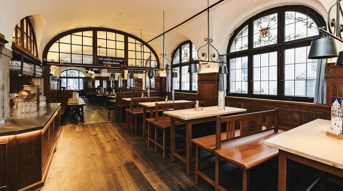 Gewölbter Gastraum mit Holzvertäfelung, Fenstern und Holztischen im Weissen Bräuhaus