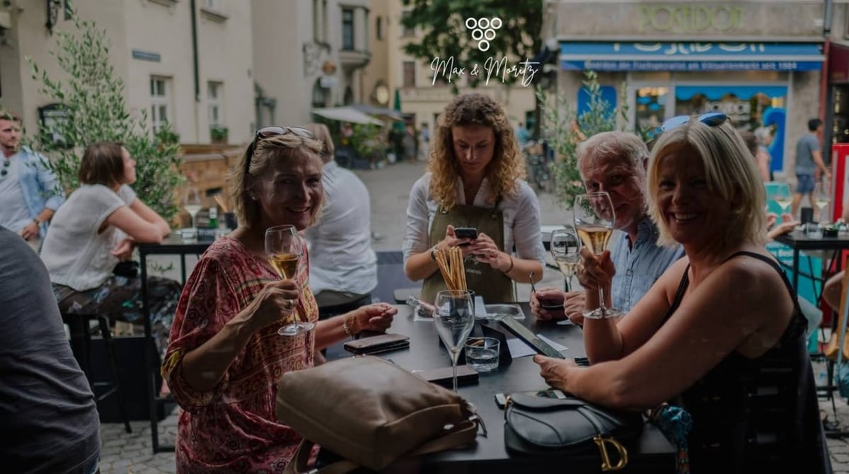 Gäste sitzen an Tischen im Freien vor der Max & Moritz Weinbar am Viktualienmarkt