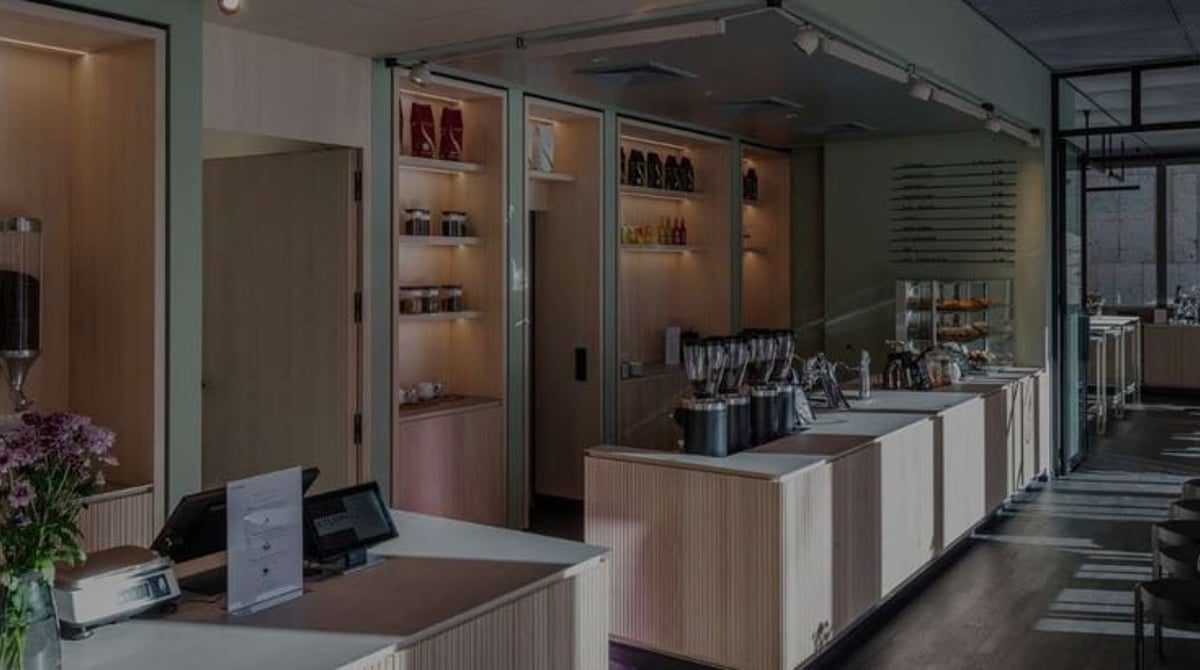 Verkaufs- und Cafébereich der Turm Barista Academy München: Holzwand mit dem Schriftzug „Turm Kaffee – seit 1761" und fünf gläsernen Bohnenspendern, davor der Kassentresen, rechts die verglaste Academy-Fläche