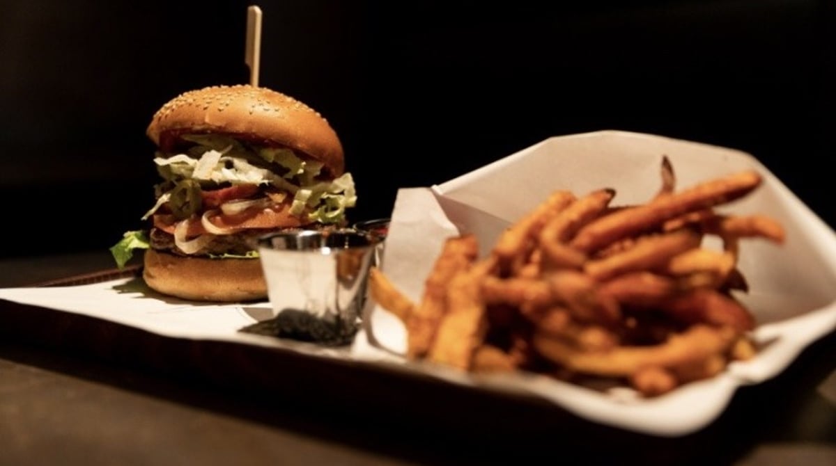 Burger mit Holzspieß und Pommes in Papier auf einem Tablett im M.C. Müller
